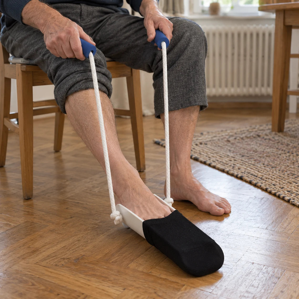 Mann schlüpft im Sitzen mit dem Fuß in den Kompressionsstrumpf auf der Mevery Anziehhilfe